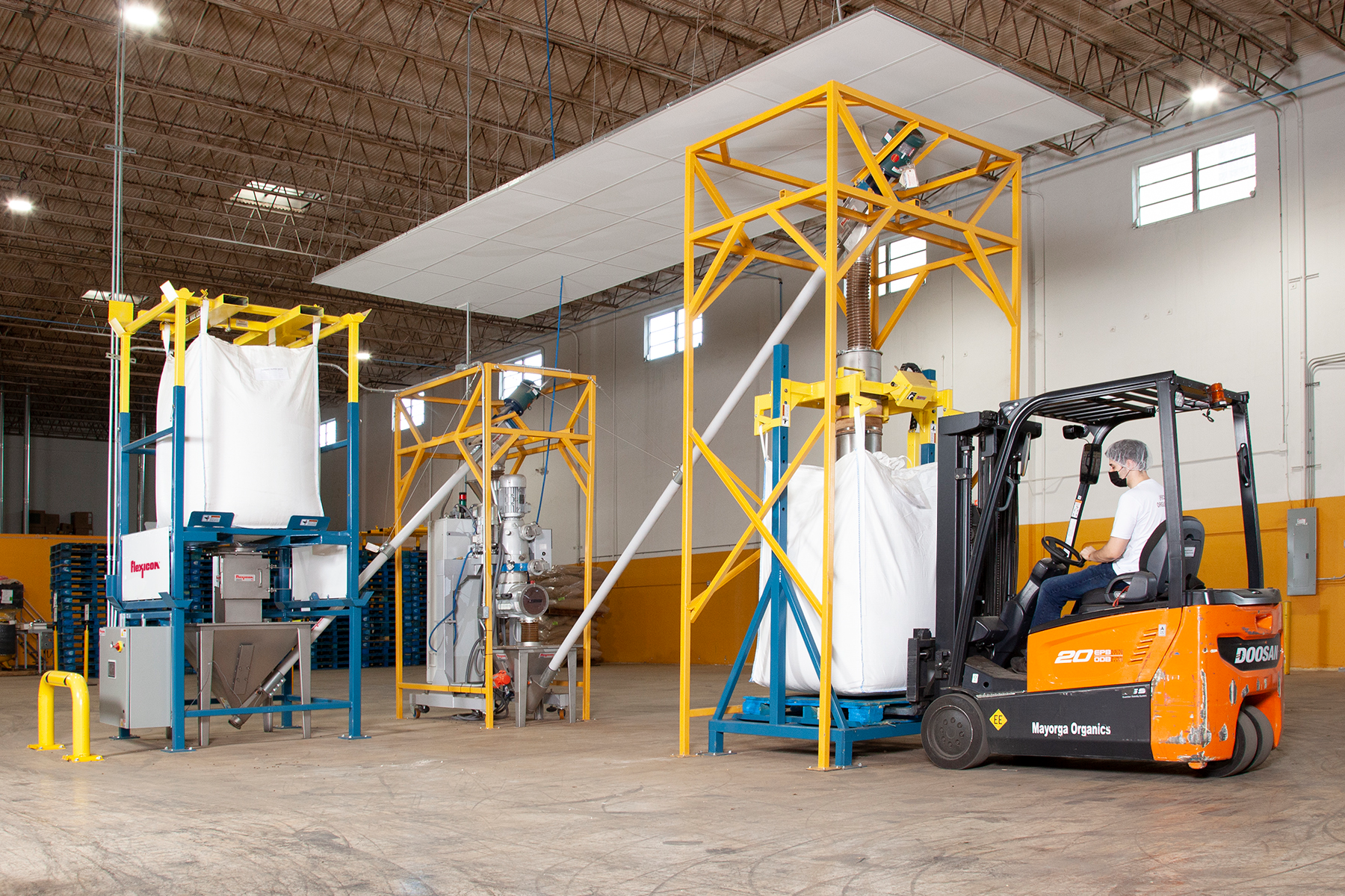 The flexible screw conveyor at left transfers roasted coffee beans from the bulk bag discharger to the grinder, while the conveyor at right moves ground coffee to the bulk bag filler.