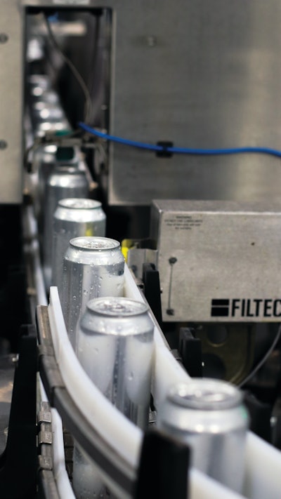 Filled and seamed bright stock cans get a Filtec fill-level check prior to date coding and labeling.
