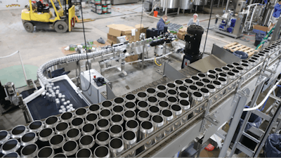 Brightstock cans are depalletized overhead on a high-trim Ska Can-i-Bus, then single-filed and lowered through a twist rinser on the way to the filler and seamer.