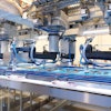 Collating F4 SCARA robots near the end of the infeed belt pick product as it travels to the right. Note the amount of product has dwindled compared to the 34 x 4 format at the start of the infeed. Groups of three sticks are collated on the narrower belts that travel to the left. Finally, cartons that have been filled and lidded upstream travel to the right, and out of the system.