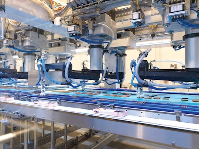 Collating F4 SCARA robots near the end of the infeed belt pick product as it travels to the right. Note the amount of product has dwindled compared to the 34 x 4 format at the start of the infeed. Groups of three sticks are collated on the narrower belts that travel to the left. Finally, cartons that have been filled and lidded upstream travel to the right, and out of the system.