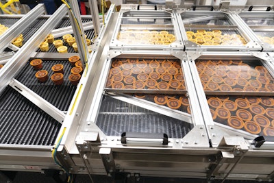 Before cups reach the Morrison timing screws that upend them and group them into stacks of six, cups exit spiral blast freezers—one for chocolate, one for vanilla—at an overhead level and move through this accumulation table that singulates the cups into two single-file rows, one chocolate and one vanilla.