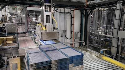 This gantry style robot picks reusable plastic trays of batteries from a pallet one tray at a time and places them on a conveyor belt leading to a station where batteries are picked from trays.
