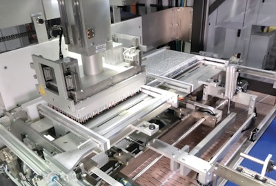 This gantry-style robot uses a magnet to pick one entire tray load of batteries from a tray and place the batteries on one of four tilt platforms.