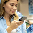 Woman in blue shirt checking smartphone near water bottle in store aisle