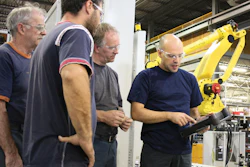 Industrial workers examining machinery near a yellow robotic arm in manufacturing facility