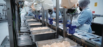 Cafe Spice production line featuring Chef Robotics’ AI-enabled arms depositing rice into dual-compartment trays. Robots work in tandem with line staff, ensuring precise placement and maintaining packaging presentation standards critical to retail-ready meals.