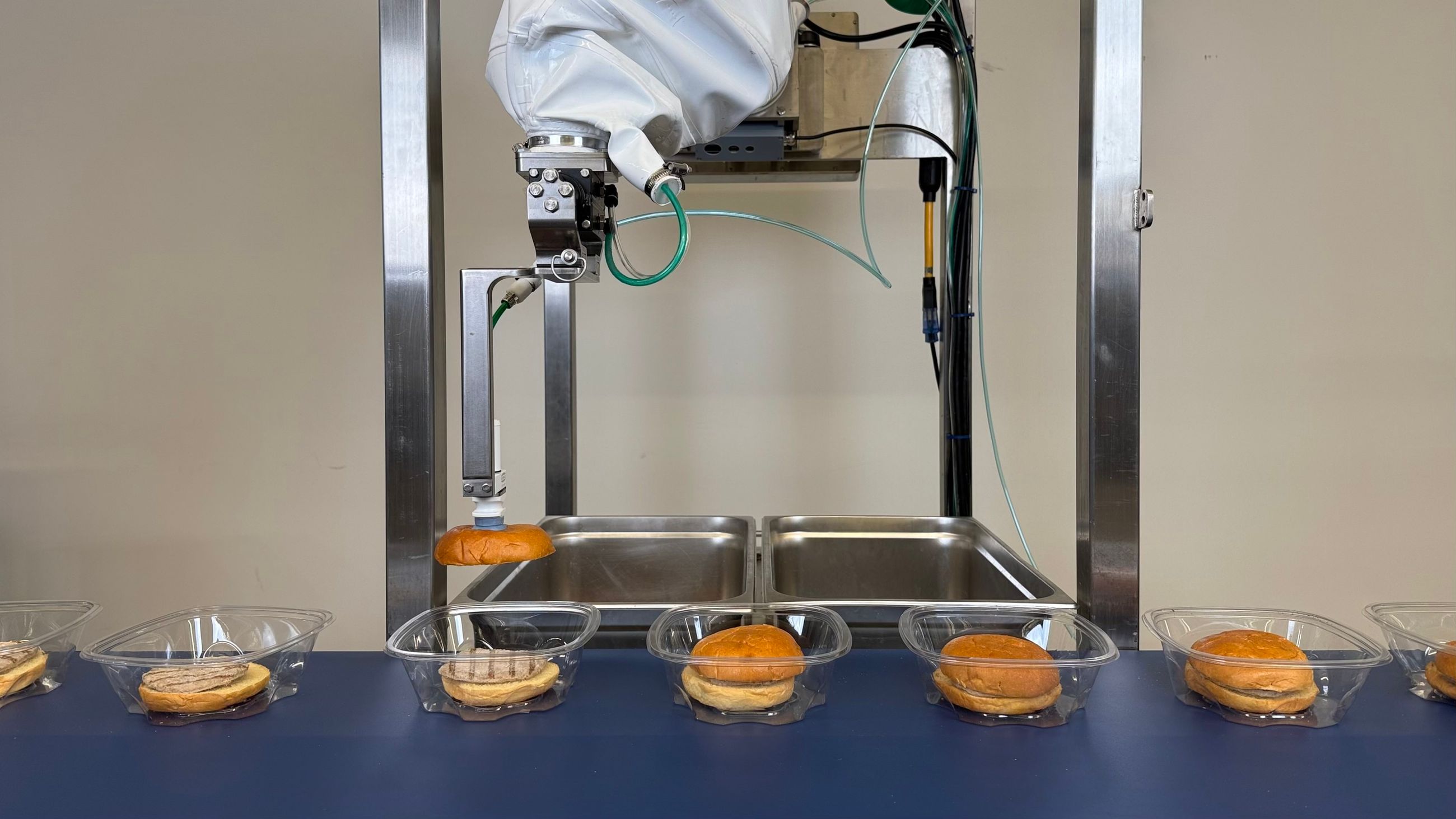 Robotic arm placing hamburger buns on metal trays in automated food processing setup