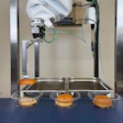 Robotic arm placing hamburger buns on metal trays in automated food processing setup