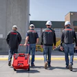 Four construction workers in safety gear walking with red equipment case