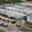 Aerial view of large industrial manufacturing facility with parking lot and surrounding green landscape