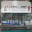 Laub-Hunt Packaging Systems industrial filling machine with white bottles on blue conveyor in factory