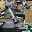 Industrial robotic arm in manufacturing facility with machinery and cardboard boxes