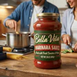 Couple cooking together in kitchen with Bella Vita marinara sauce jar and fresh ingredients on wooden counter