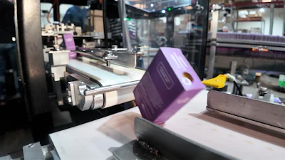 Filled cartons with soap roll off the cartoning machine for packing.