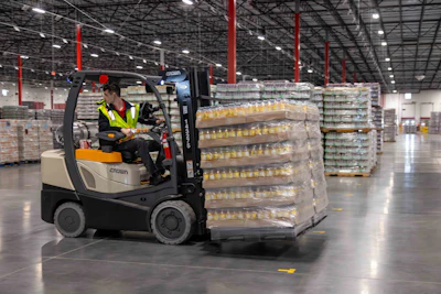 A stretch-wrapped pallet moves through a Coca-Cola Consolidated distribution facility. Proper load containment at this stage — the product of calibrated wrap recipes maintained across more than 70 wrappers in 11 plants — is what separates a clean delivery from a down-load.