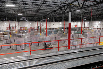 Properly contained pallets stage in a Coca-Cola Consolidated warehouse awaiting shipment. A 'down-load' — a pallet that topples in transit or in the warehouse — means product that cannot be sold, making load containment a direct cost issue.