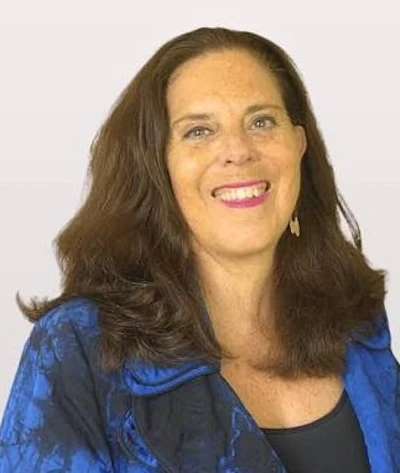 Professional headshot of a smiling woman with long brown hair wearing a blue patterned blazer