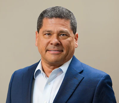 Professional headshot of a man in blue blazer and light blue shirt against neutral background