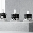 Three black industrial motors with white cylindrical tops displayed on concrete platform in modern showroom