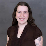Professional headshot of a smiling woman with dark wavy hair wearing a brown top and gold hoop earrings