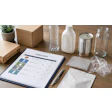 Compliance checklist document on desk surrounded by recyclable containers, glass jars, and sustainable packaging materials
