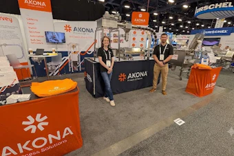AKONA trade show booth with orange branding, staff members, and company signage at exhibition event