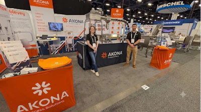 AKONA trade show booth with orange branding, staff members, and company signage at exhibition event