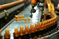 Industrial robotic arm dispensing liquid into amber bottles on a production line conveyor system