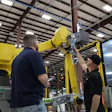 Two technicians service a yellow FANUC industrial robotic arm in a warehouse facility