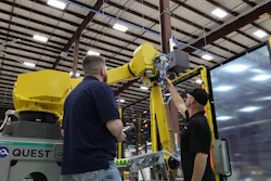 Two technicians service a yellow FANUC industrial robotic arm in a warehouse facility