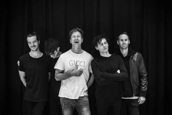 Five men posing together against dark curtain backdrop in black and white photograph