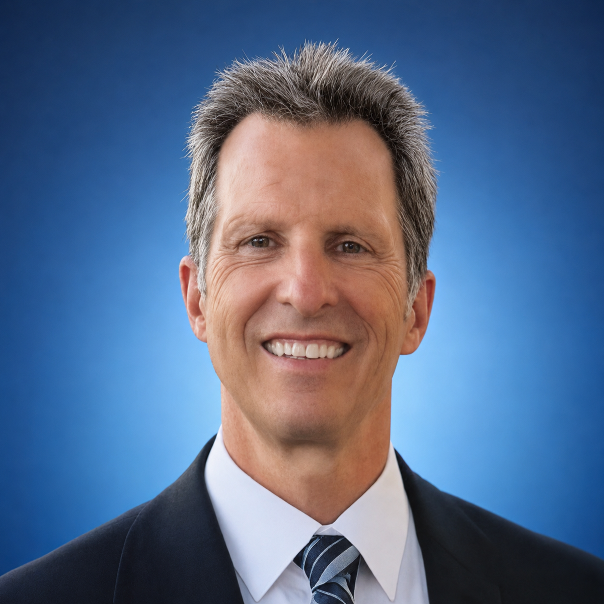 Professional headshot of a smiling man in business attire against a blue background
