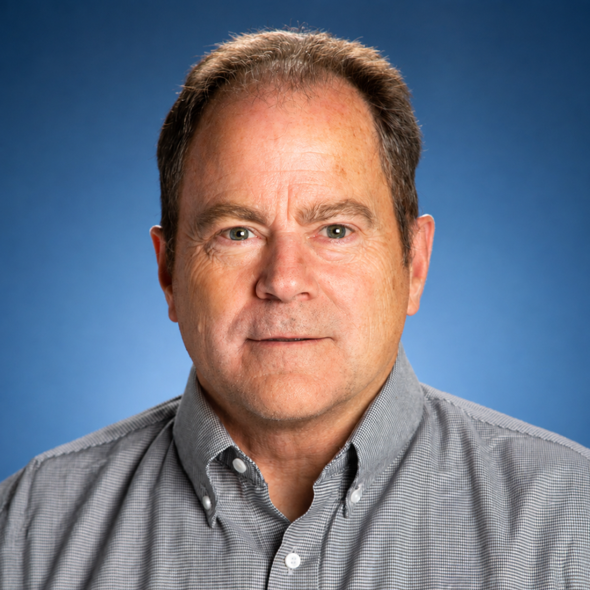 Professional headshot of a man in a gray button-up shirt against a blue background