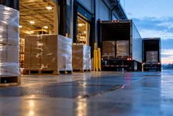 Warehouse loading dock at dusk with wrapped pallets and trucks lined up for shipment