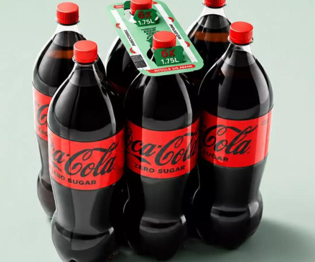 The alternative format holds individual PET bottles together using strategically positioned adhesive dots, with a rigid cardboard carrying handle fitted to the assembled pack.