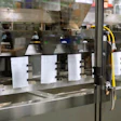 Industrial production line with white containers and metal equipment visible through glass enclosure