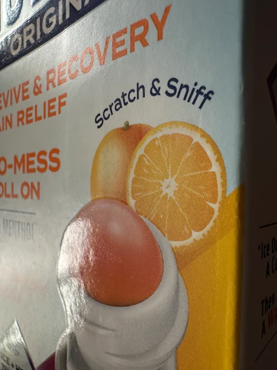 Spot gloss picks out the rollerball graphic against the matte carton face. The scented varnish that carries the fragrance is clear and sits on the same printed panel.