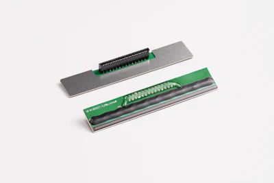 Thermal printer head components showing metal plate and green circuit board assembly