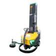 Industrial stretch wrap machine with yellow hood, dark gray mast, green accents, and ground-level wrapping attachment