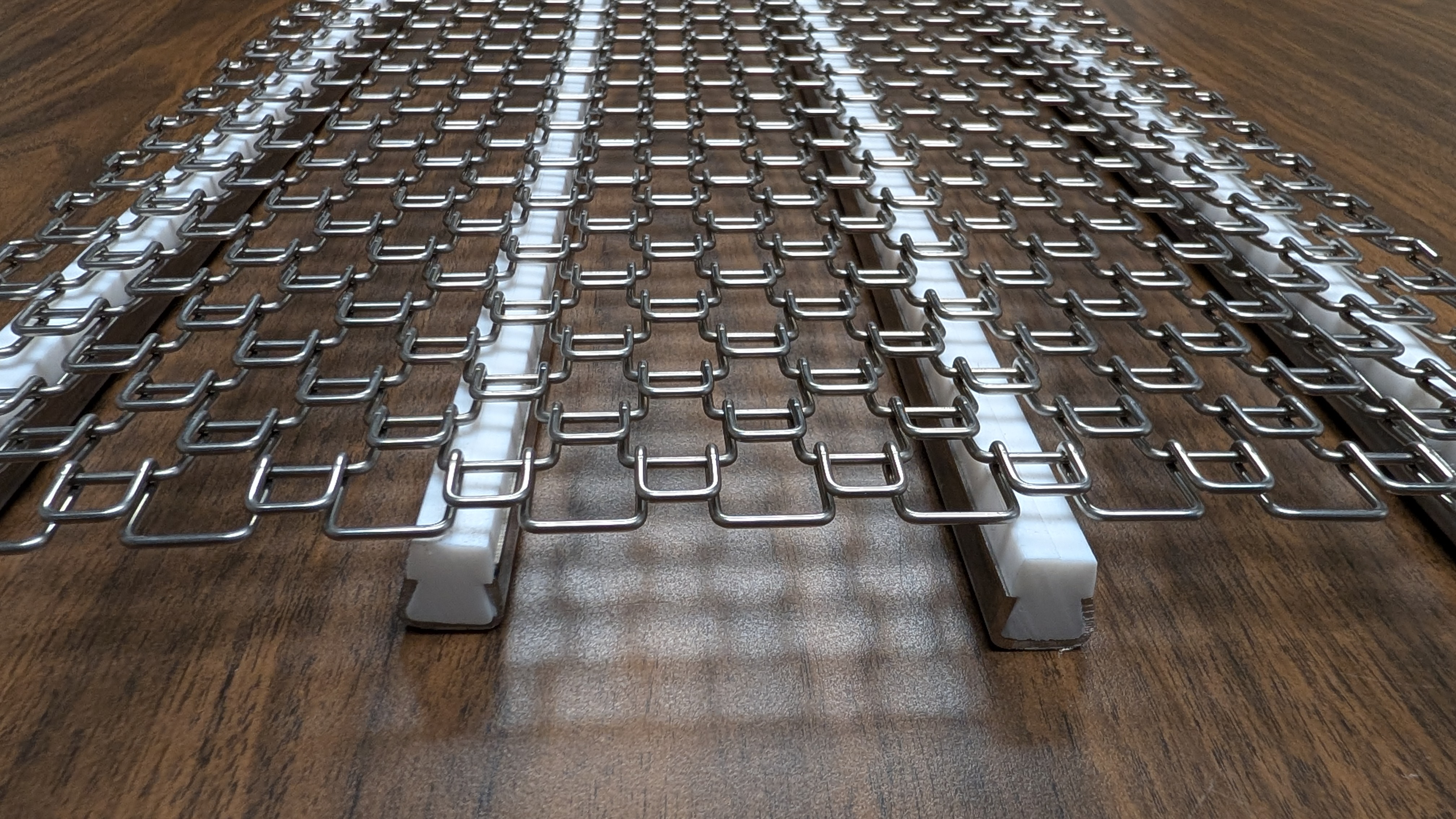 Industrial metal mesh grating with repeating square pattern installed on wooden flooring, viewed from above at an angle