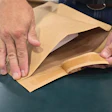 Hands opening a kraft paper envelope on a gray work surface