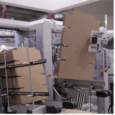 Industrial manufacturing facility with cardboard boxes on conveyor system and white machinery equipment