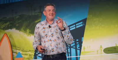 Man in patterned shirt presenting on stage with colorful backdrop and geometric design elements