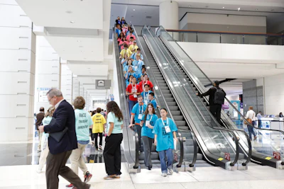 Crowded escalator in modern convention center with attendees wearing blue event shirts