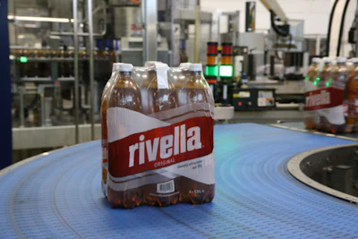 Rivella Original beverage bottle pack on blue conveyor surface in manufacturing facility