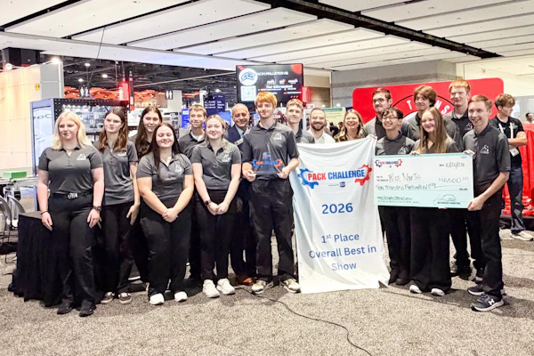 Team members in black uniforms celebrate first place at PACK Challenge 2026 robotics competition with banner.