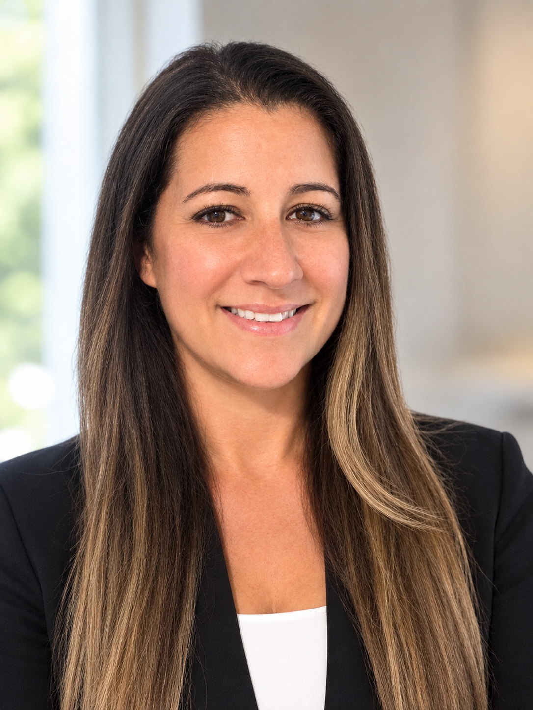 Professional headshot of a woman with long dark hair wearing a black blazer and white top, smiling at the camera