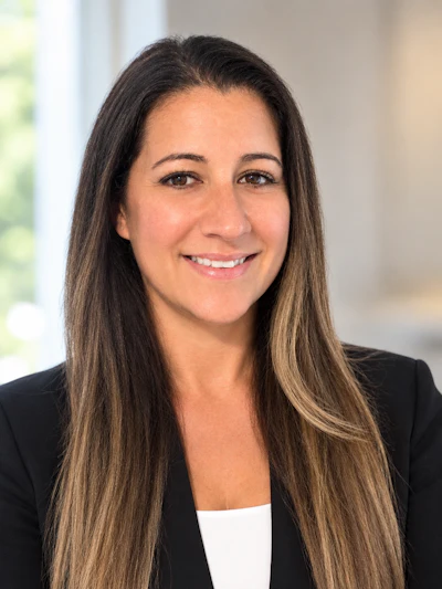 Professional headshot of a woman with long dark hair wearing a black blazer and white top, smiling at the camera