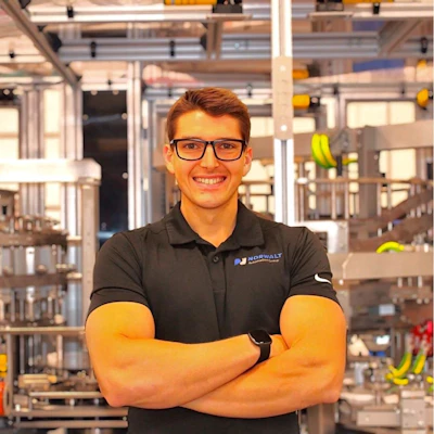 Young man in glasses wearing black HORWALT polo shirt, smiling with arms crossed in modern warehouse setting